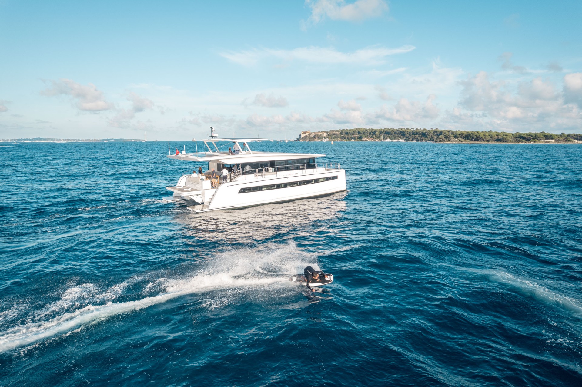 Aerial view of a rider on an Awake RÄVIK electric jetboard carving behind a motor catamaran